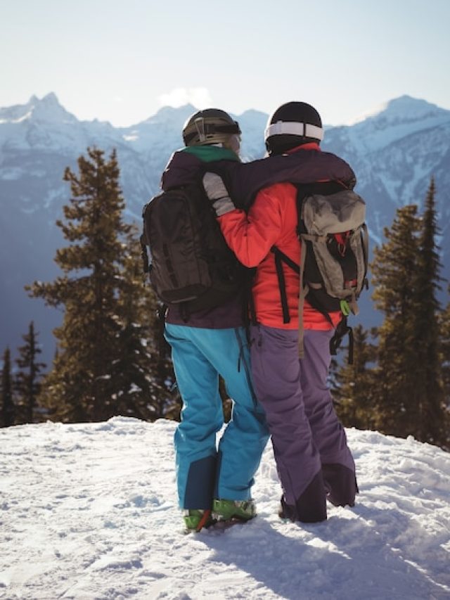 two-skiers-standing-together-with-arm-around-snow-covered-mountain_107420-96442